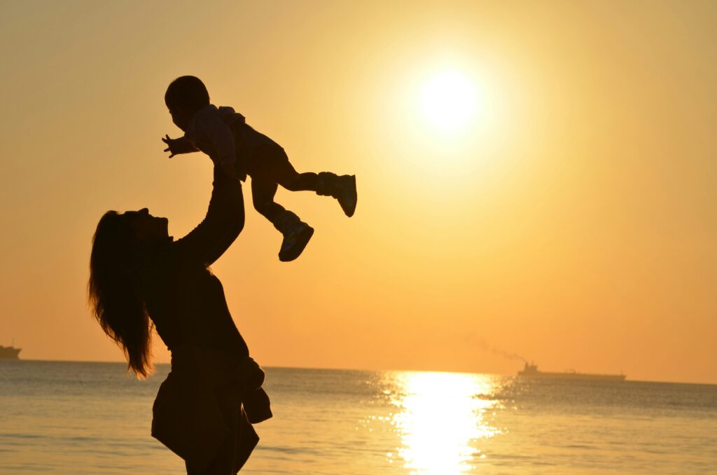 A silhouette of a woman lifting a small child in the air at the beach during a golden sunset